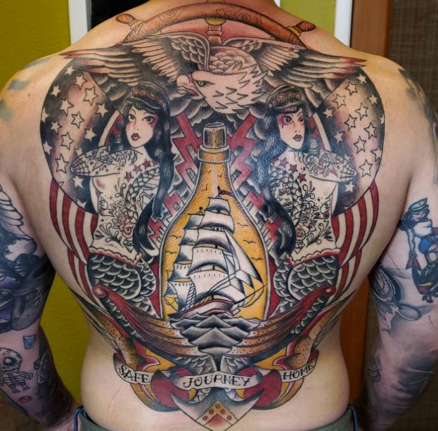 Back mural tattoo of ship in a bottle with tattooed mermaid ladies, eagle flying above, american flag. Safe journey home